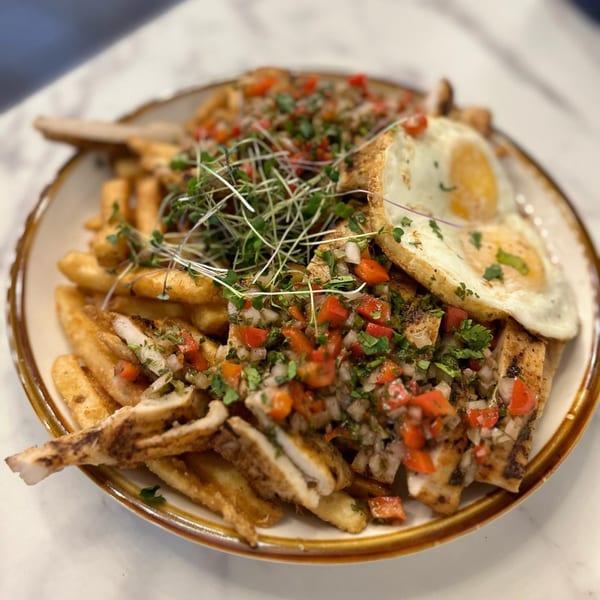 Latin-American dish with fries, grilled chicken, pico de gallo, microgreens, and two fried eggs.