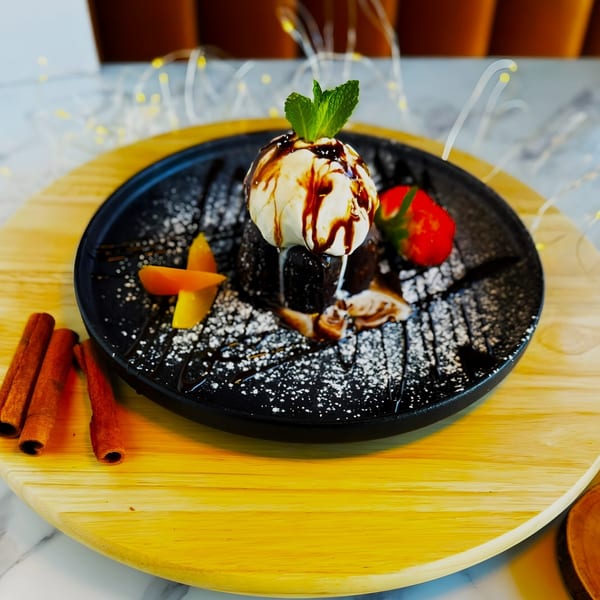 Chocolate lava cake with vanilla ice cream, mint, strawberry, and mango on a black plate.
